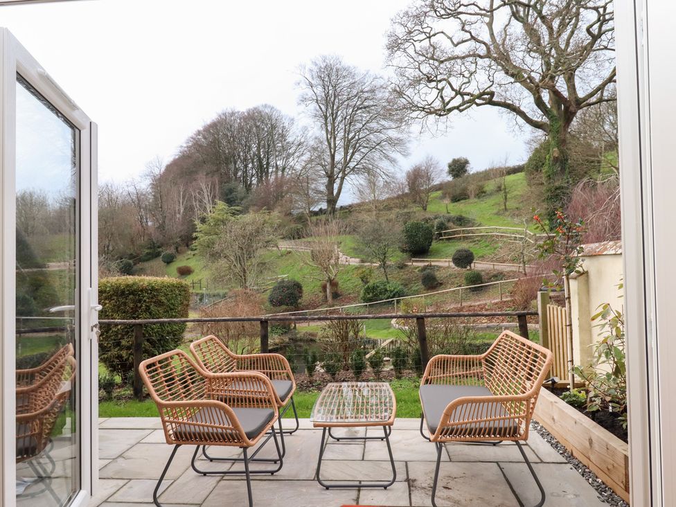 A patio area with chairs and a table overlooking a garden at Garden Cottage at the Bowden Estate Stoke Fleming