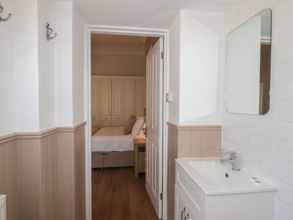 A bathroom with a sink and mirror looking into a bedroom at Flat 2 The Moorings in Torquay
