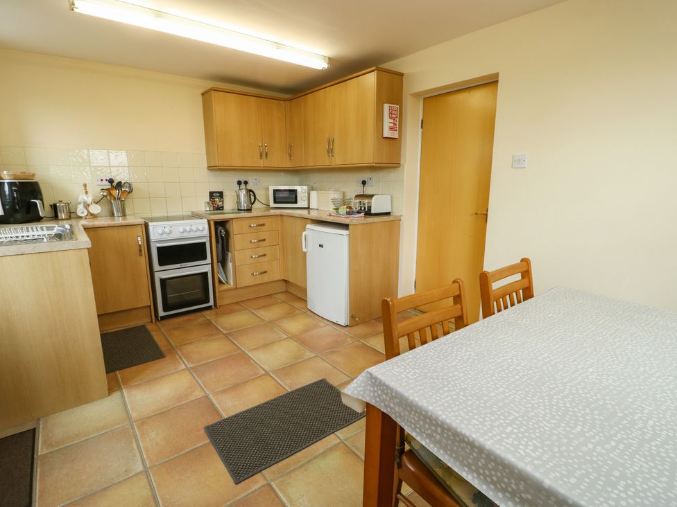 A kitchen with oven, sink, microwave, and table with chairs at Getws in Ty Croes