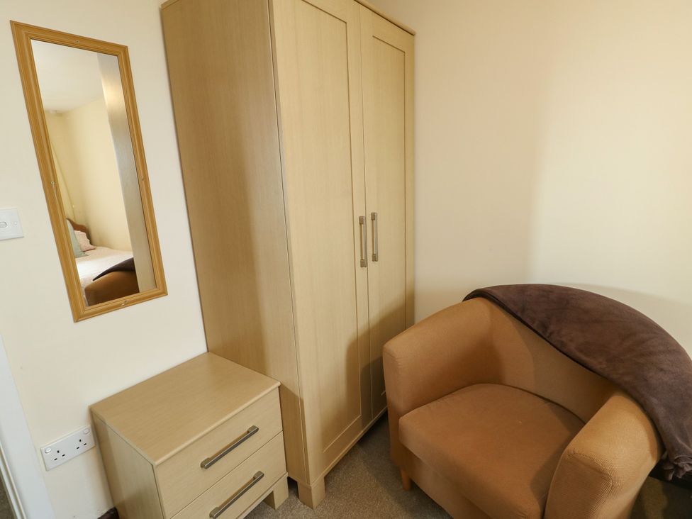 A bedroom with a wardrobe, mirror, nightstand, and chair at Getws, Ty Croes