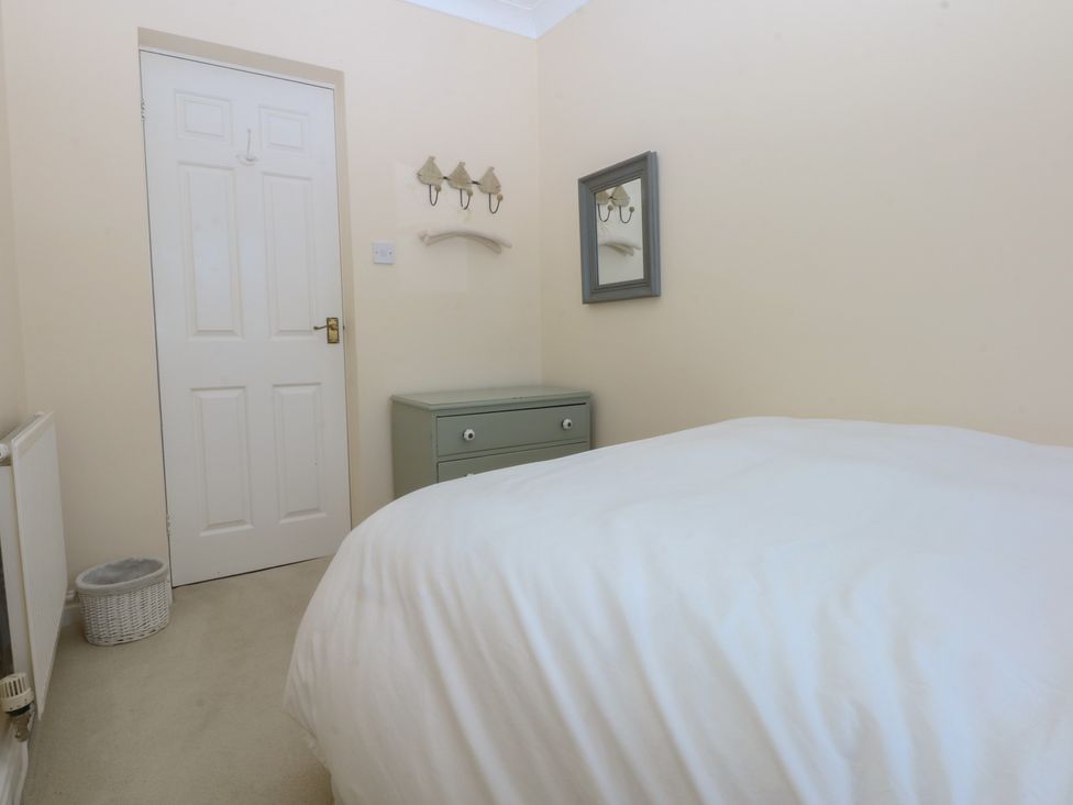 A bedroom with a bed, chest of drawers, mirror and coat hooks at 15 Rose Hill Beaumaris