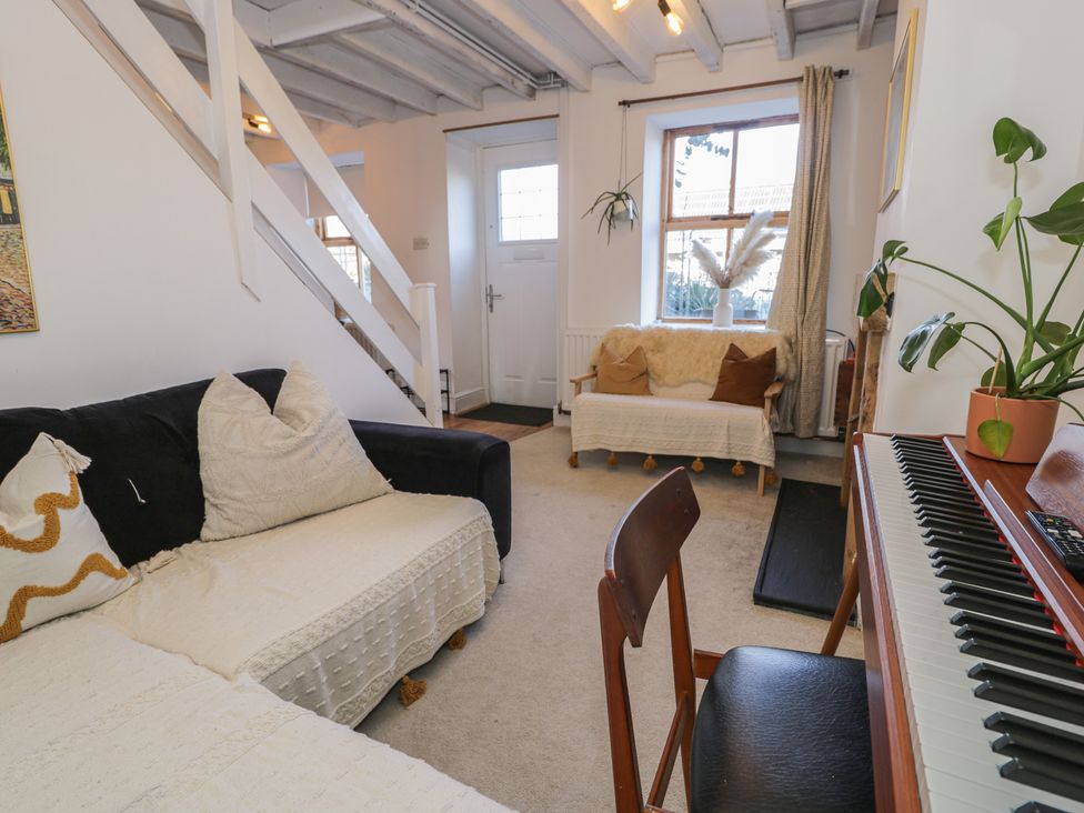 A living room with a sofa, piano, and chair at Lon Popty in Dolgellau