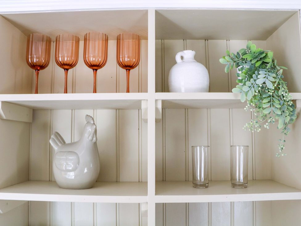 A kitchen shelf with glasses, a pitcher, a chicken figurine, and a decorative plant at Farm View Annex, Painswick