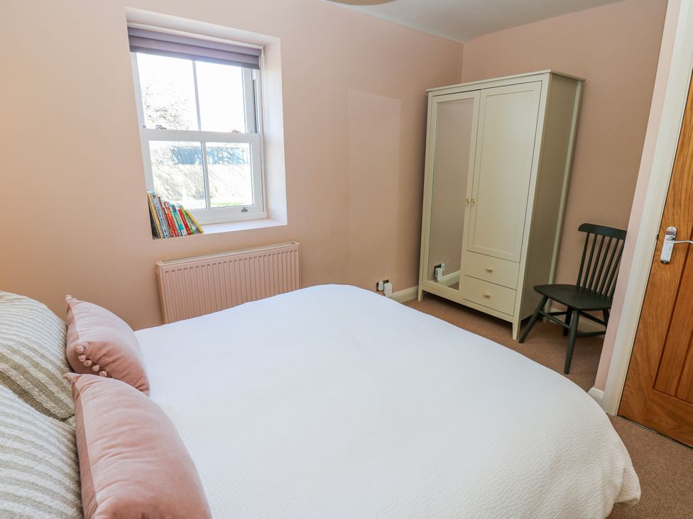 A bedroom with a bed, wardrobe, chair, and books at 27 West Green