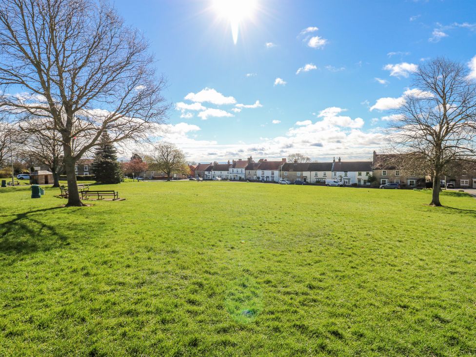 A green field with trees and houses in the background at 27 West Green 