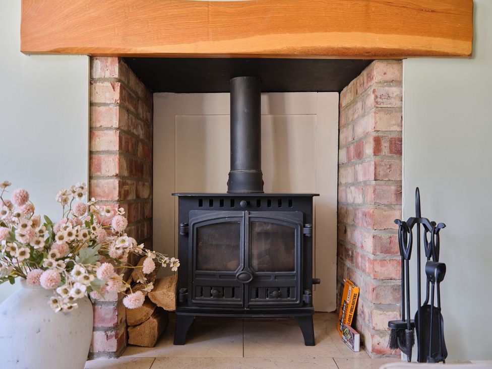 A living room with a wood stove and logs at 27 West Green in Heighington