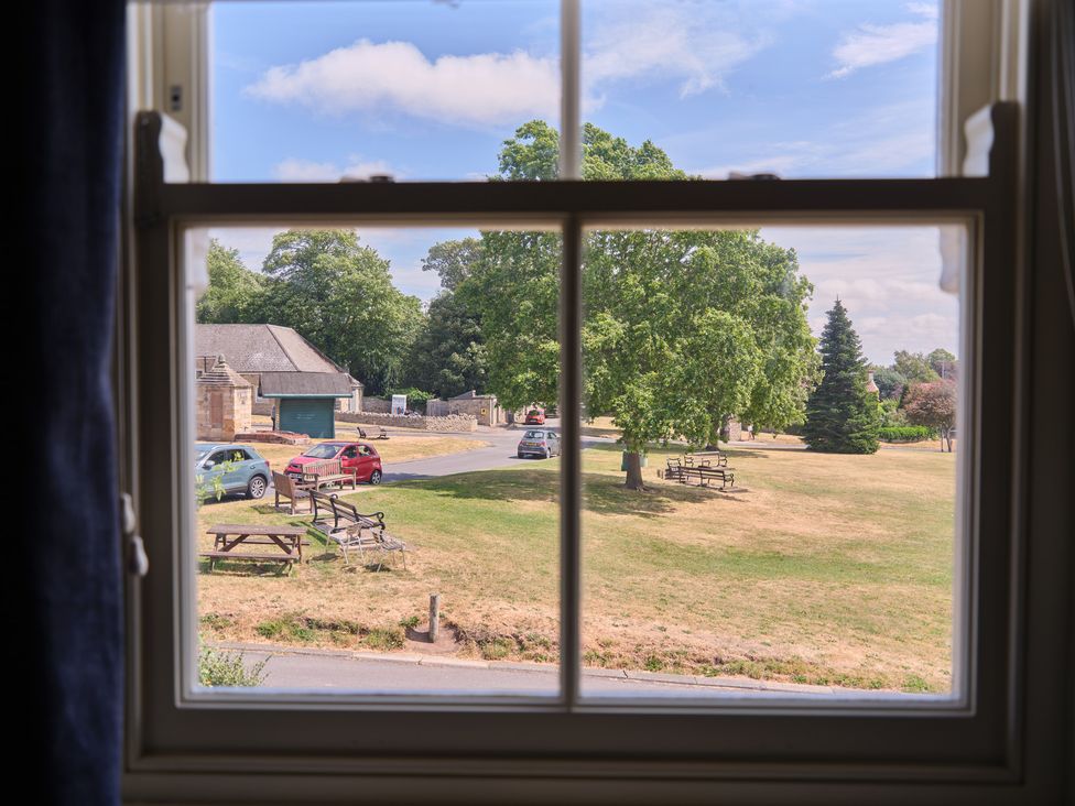 A view of a park with trees and cars from a window at 27 West Green in Heighington