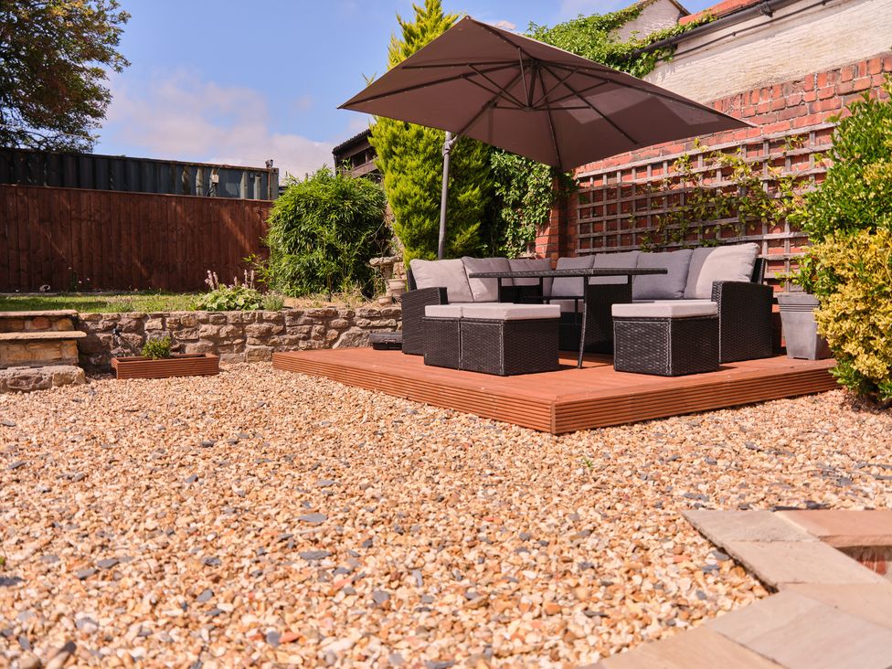 A garden with gravel, outdoor seating, a table, and a parasol at 27 West Green in Heighington