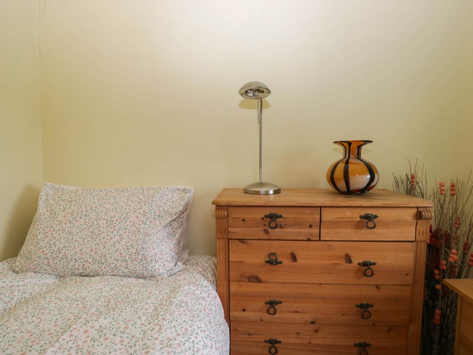 A bed with floral bedding next to a wooden chest of drawers and a lamp at The Spinney near Milnthorpe