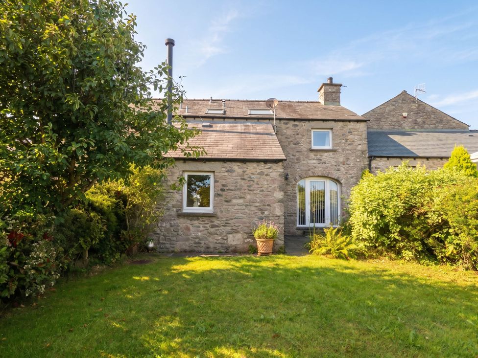 A stone house with a garden and trees at The Spinney near Milnthorpe