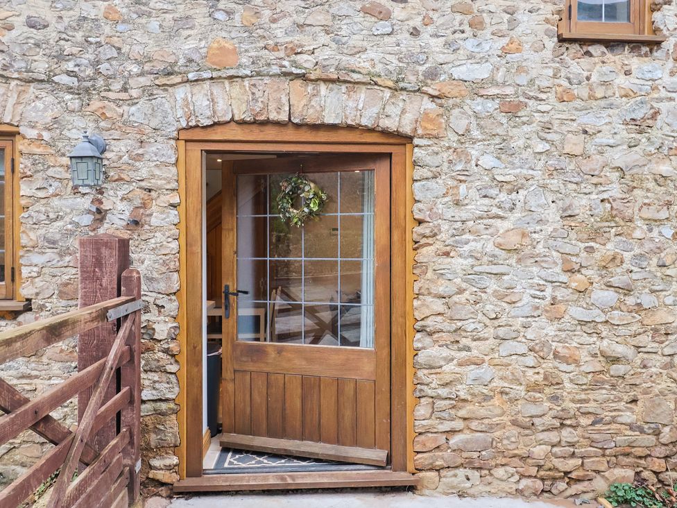An entrance door with a stone wall and light fixture at Rose Cottage in Wellington