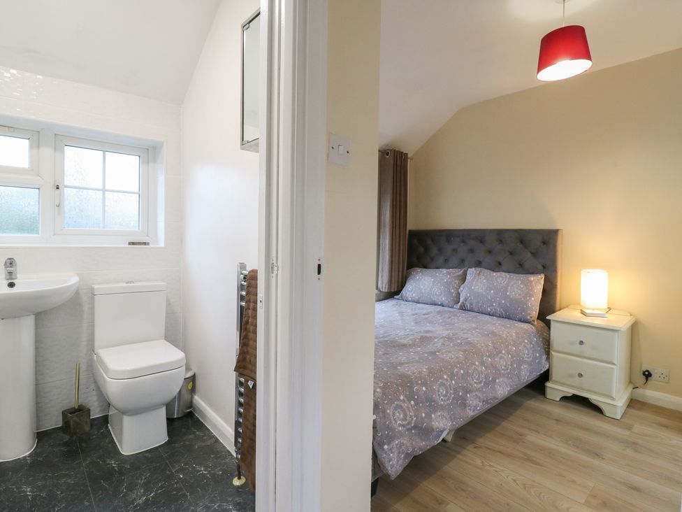 A bathroom with sink and toilet adjacent to a bedroom with a bed and nightstand at Headmasters Hollow in Watford