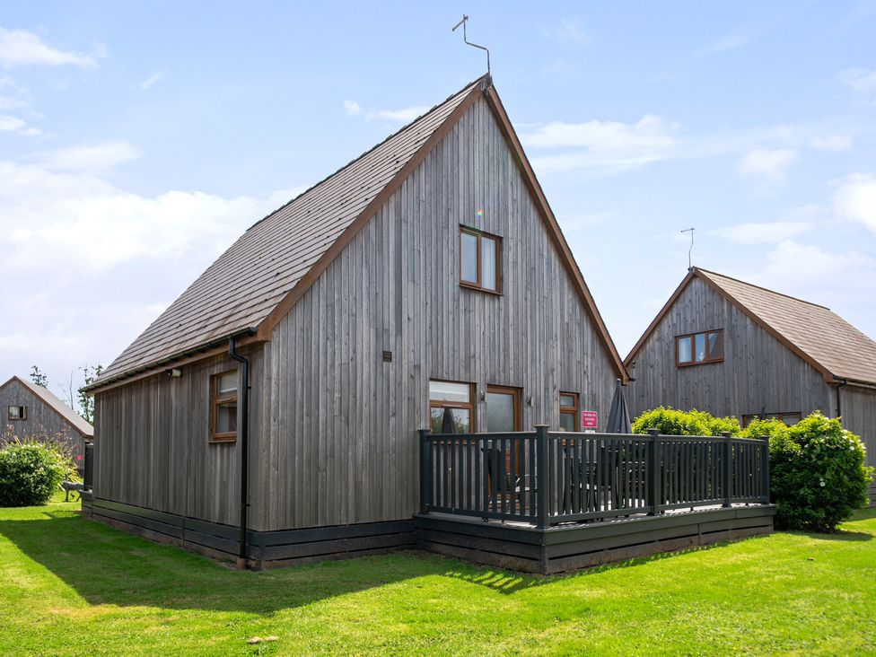 A wooden cabin with a deck and grass outside at James Ville Marina Lodge 8 Brigg