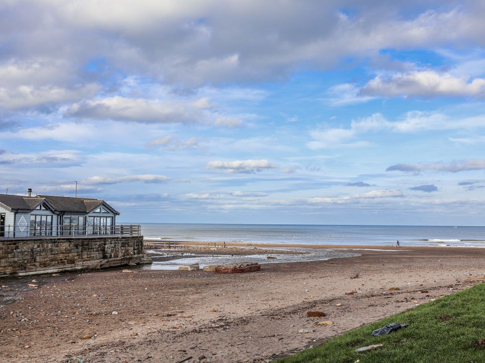 A beach with buildings by the water at South Villa Sandsend near Whitby