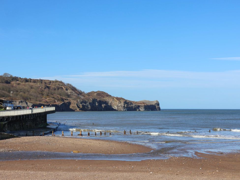 A beach with a cliff and a pier at South Villa in Sandsend near Whitby