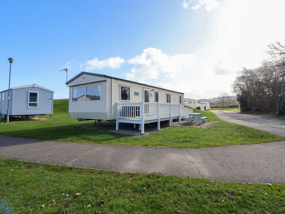 A mobile home with a deck and table at Dunes View in Prestatyn
