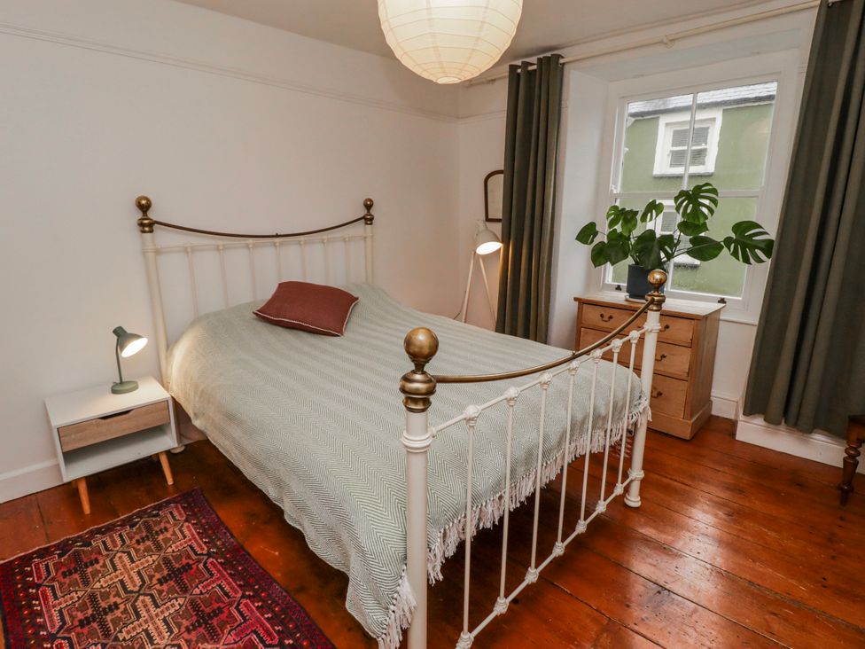 A bedroom with a bed, nightstand, lamp, dresser, and plant at The Secret Garden in Narberth