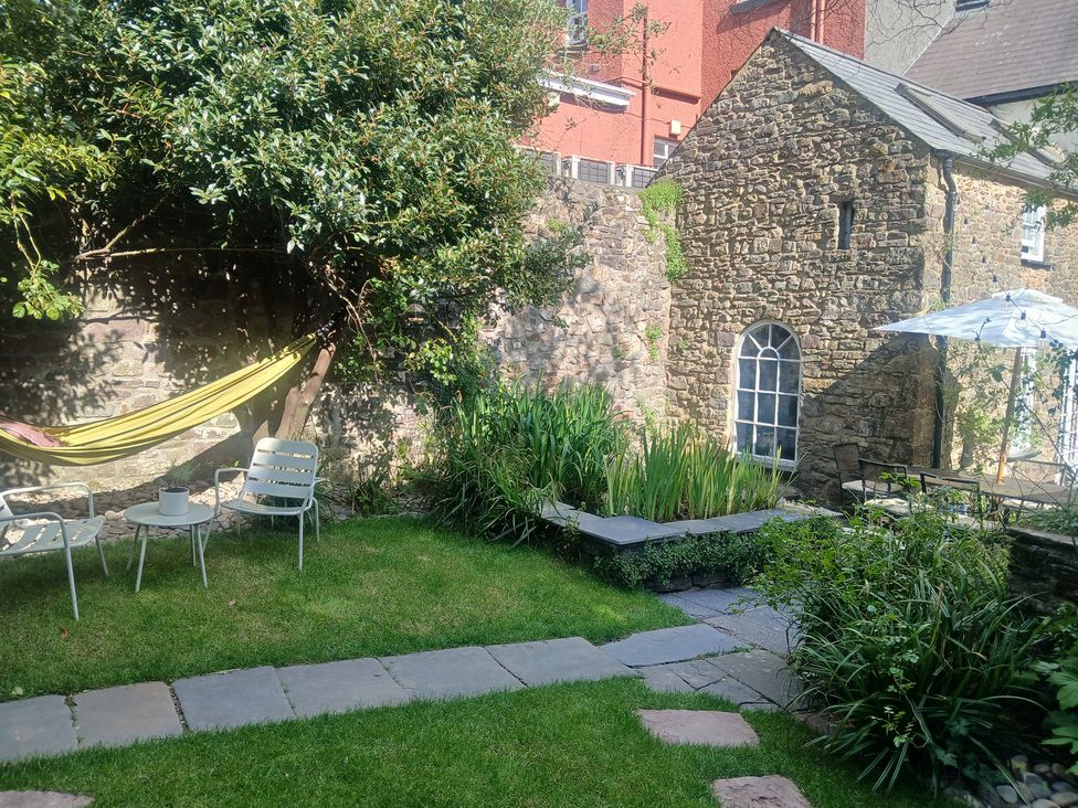 A garden with a hammock, chairs, and a stone wall at The Secret Garden in Narberth