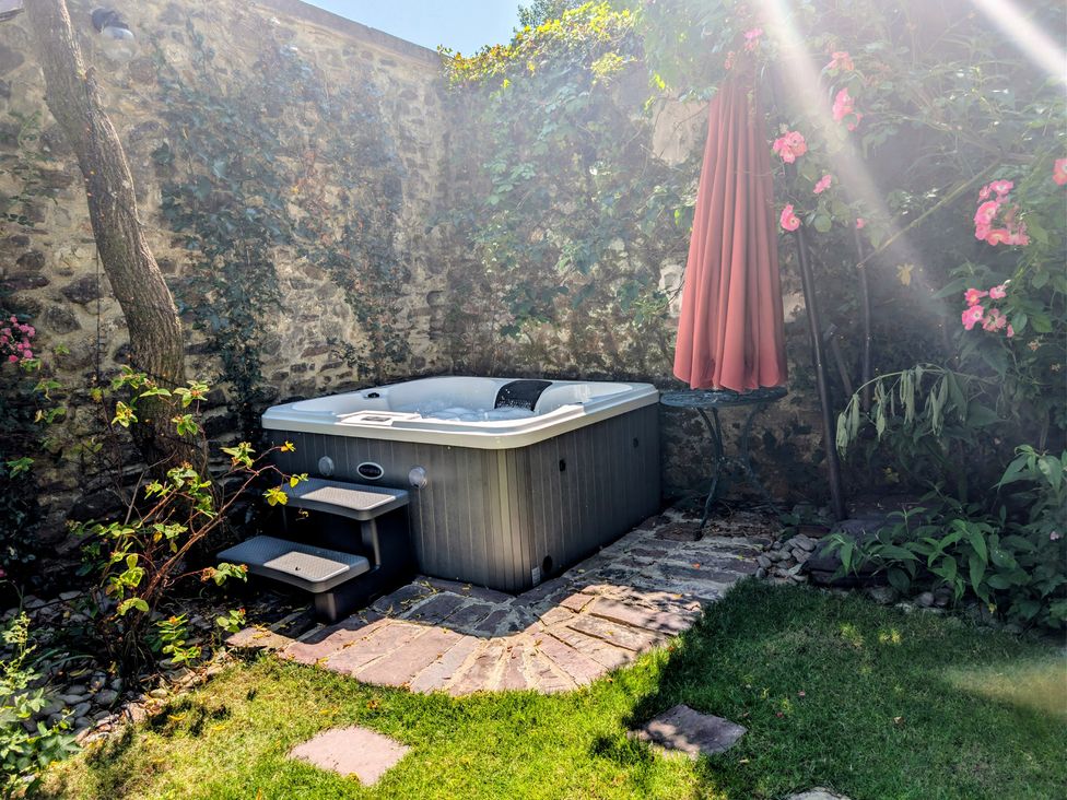 A garden with a hot tub and a table with an umbrella at The Secret Garden in Narberth