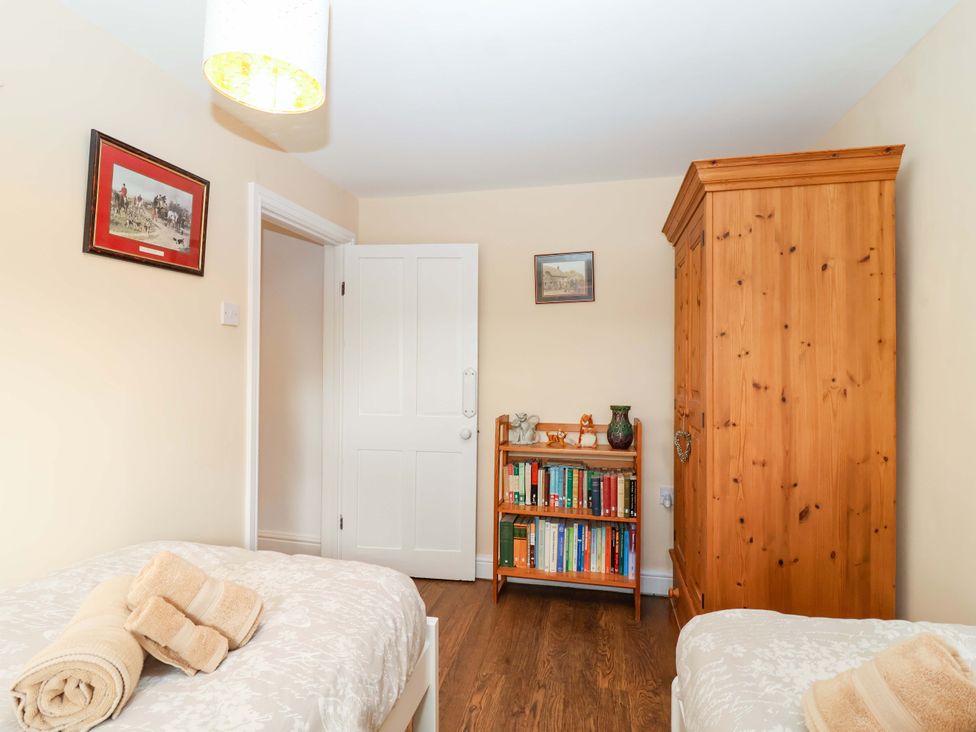 A bedroom with two beds, wardrobe, bookshelf, and pictures at 12 Heathfield Terrace