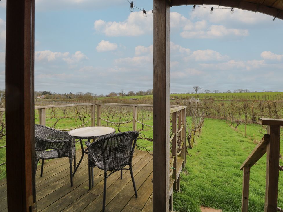 A deck with chairs and a table overlooking a vineyard at Vine View near Halesworth