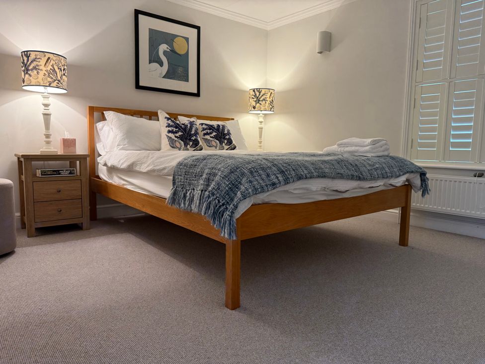 A bedroom with a bed, nightstand, and lamps at York Cottage Southwold