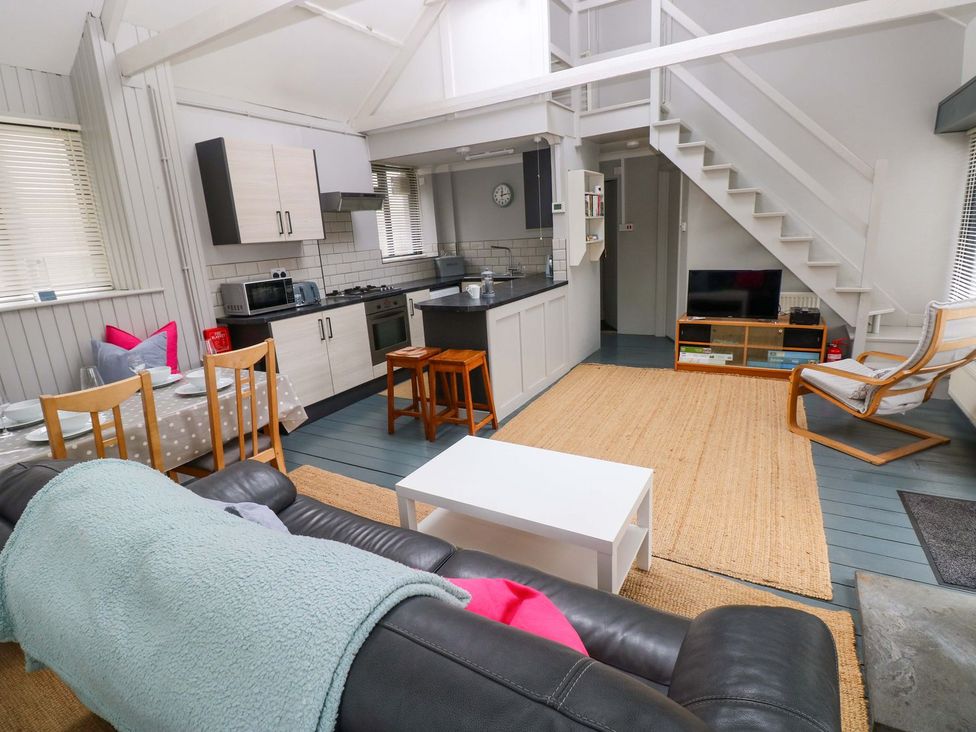 A living room with a sofa and kitchen area at Brewery Cottage