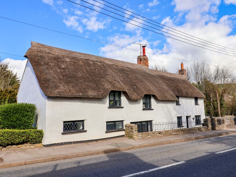 A thatched cottage with windows and a hedge at Bridge Cottage in Chideock