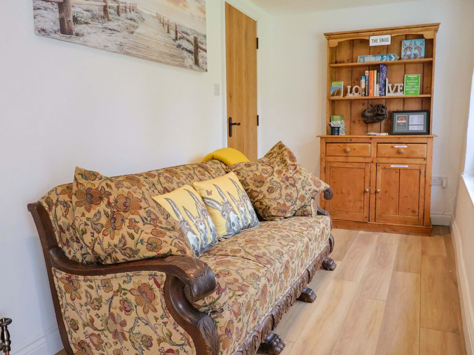 A snug with a floral sofa and a wooden bookshelf at Bridge Cottage in Chideock