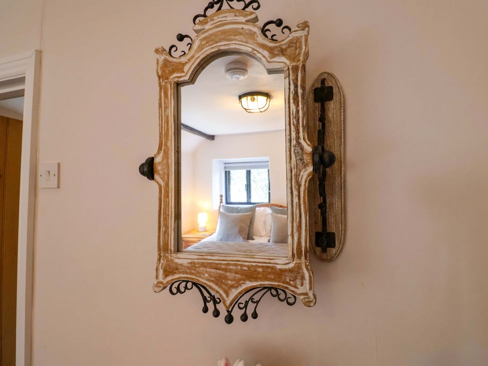 A mirror reflecting a bedroom with a bed and light at Bridge Cottage in Chideock