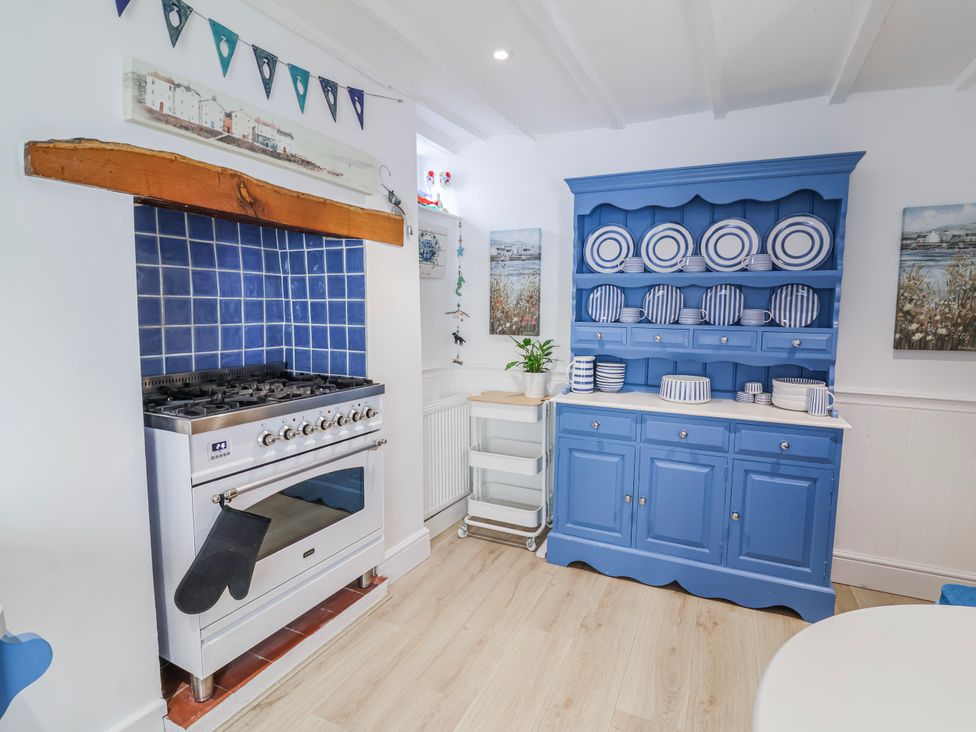 A kitchen with a stove and blue cabinet containing plates at Hideaway Cottage