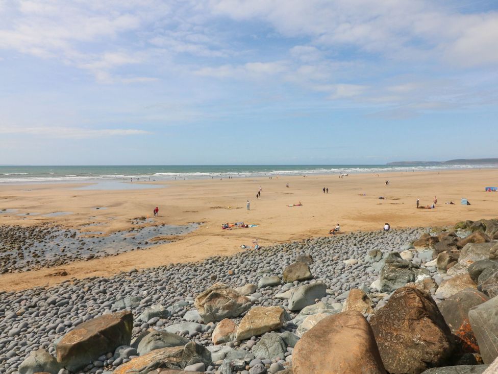 A beach scene with people walking and sitting near the water at Hideaway Cottage