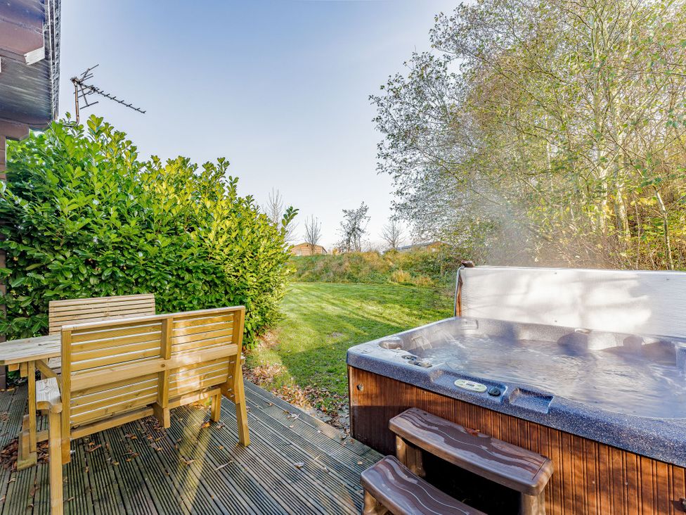 A garden with a hot tub and a wooden dining set at Poplar Lodge (Pet) Thirsk