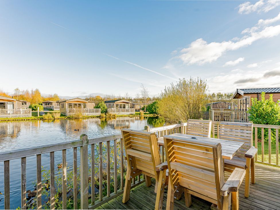 An outdoor area with chairs and a table overlooking a pond at Spruce Waterside Spa (Pet) Thirsk