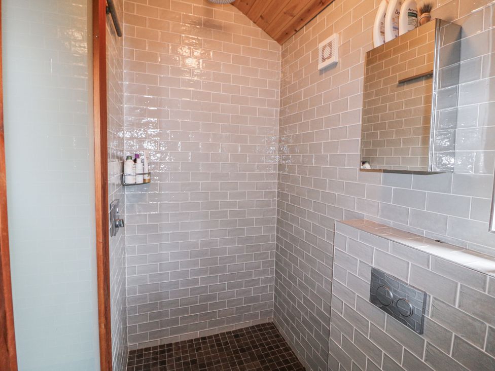 A shower with tiles and toiletries on a shelf at The Faithfuls Cabin in Dingle