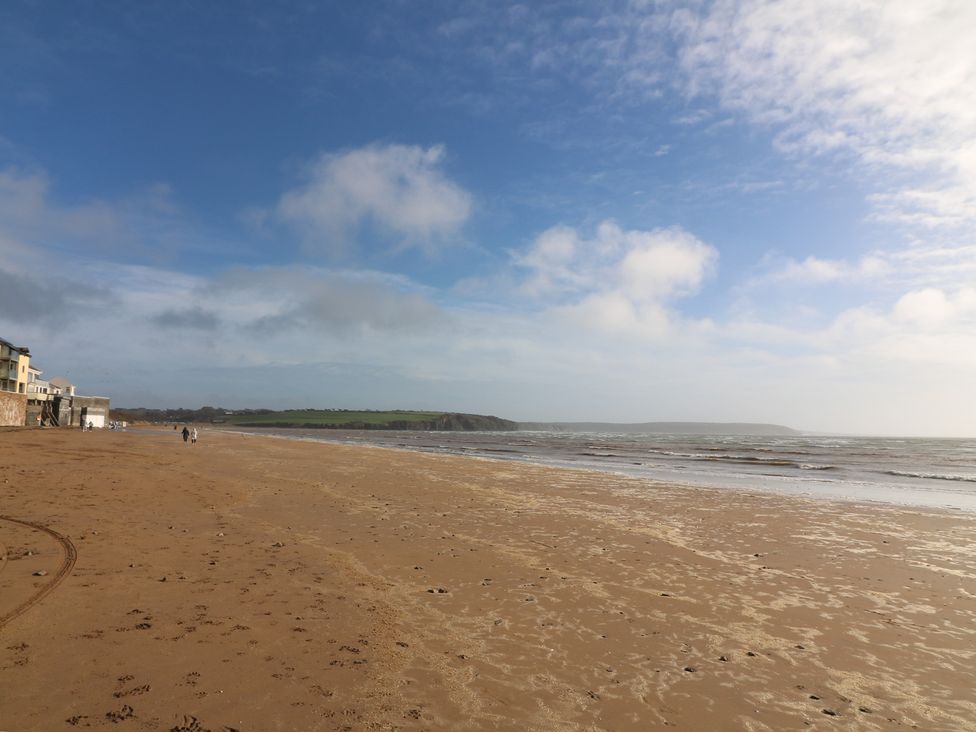 A beach with people walking and buildings along the shoreline at Radharc an Hook @ Estuary Bliss