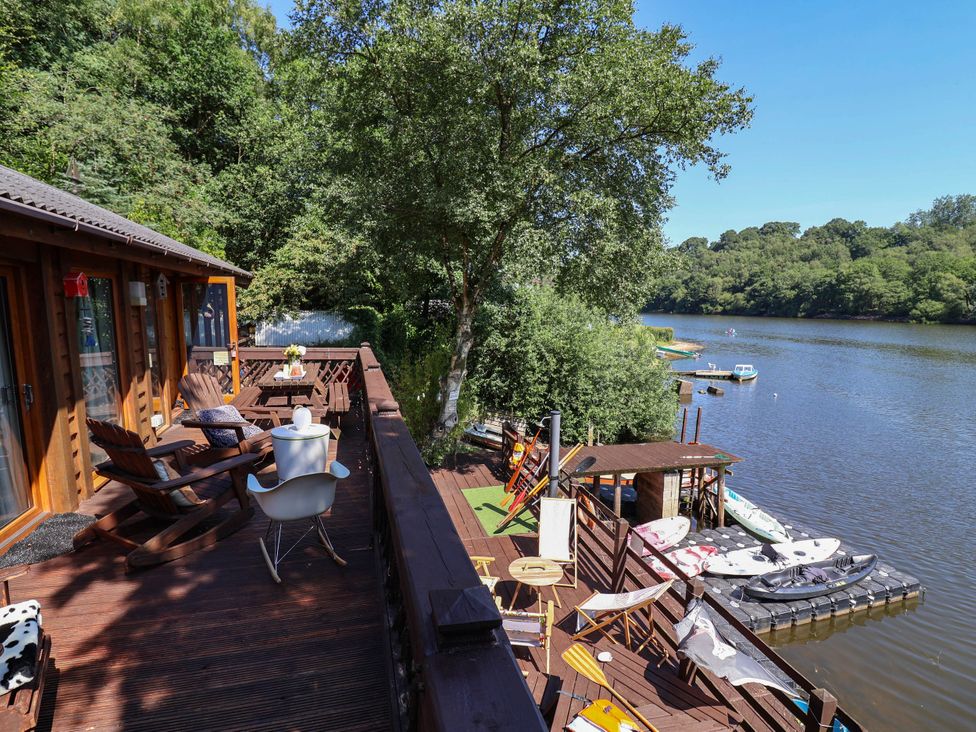 An outdoor deck with chairs and a table overlooking a river at The Boat House in Rudyard Lake