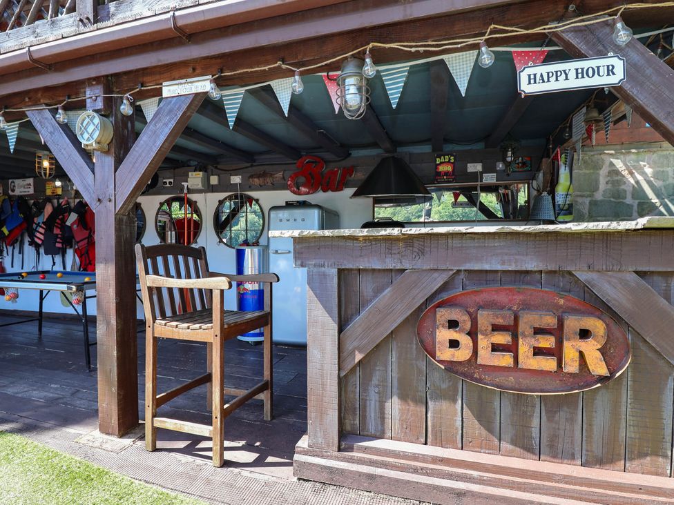 An outdoor bar area with a wooden bar and stools at The Boat House in Rudyard Lake