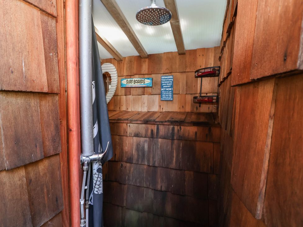 An outdoor shower area with wooden walls and a surfboards sign at The Boat House, Rudyard Lake