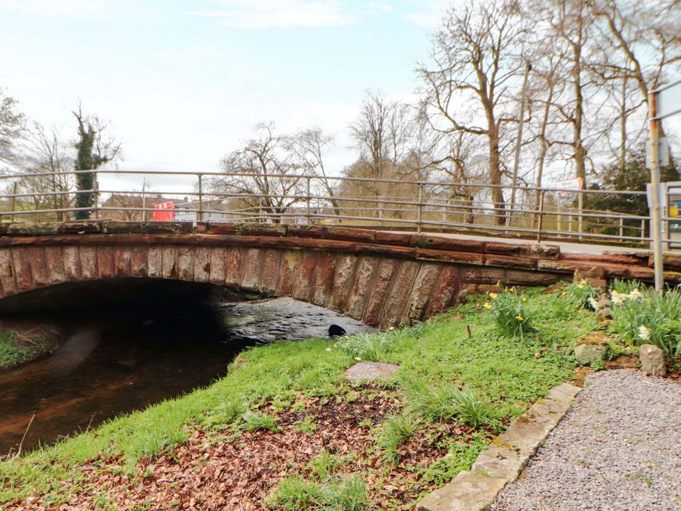 A bridge over a stream with grass and trees at The Barn in Warcop