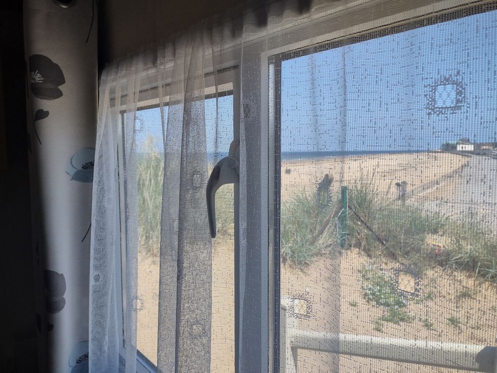 A view through a window with a curtain to a beach at Sands Retreat in Redcar