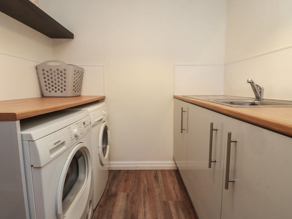 A laundry room with a washing machine, dryer, sink, and cupboards at Flat 6 in Lytham St. Annes