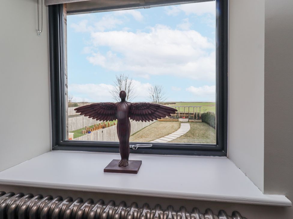 A window with a statue on the sill and a view of the outdoor pathway at The Joiners Cottage Birling near Warkworth