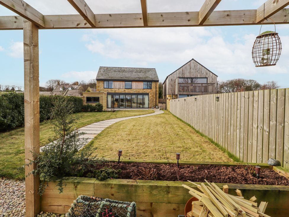 A garden with a house and pathway at The Joiners Cottage in Birling near Warkworth