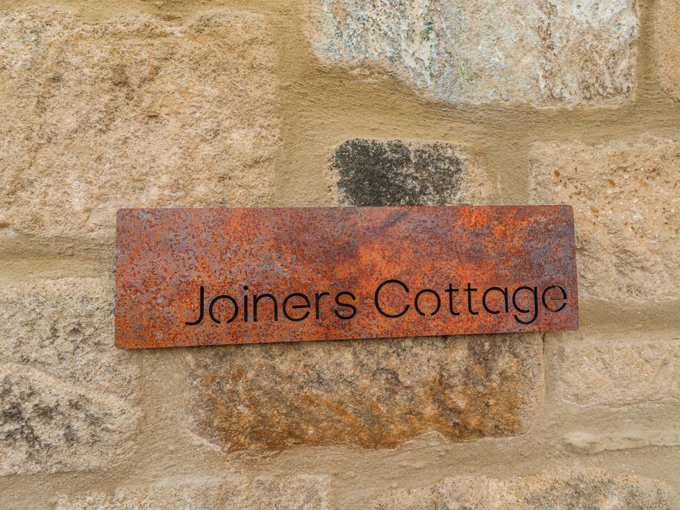 A sign reading Joiners Cottage on a stone wall at The Joiners Cottage in Birling near Warkworth