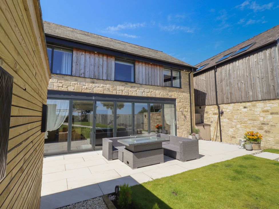 An outdoor seating area with a stone wall and glass doors at The Joiners Cottage in Birling near Warkworth