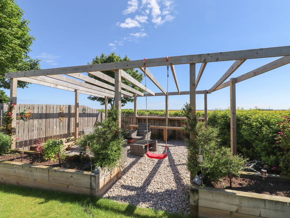 A garden with a pergola, bench, and swing at The Joiners Cottage in Birling near Warkworth