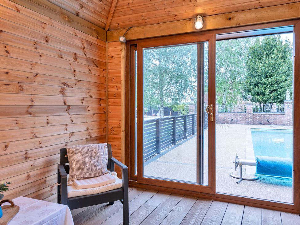 A snug with a chair and glass door opening to a pool at Oldfields