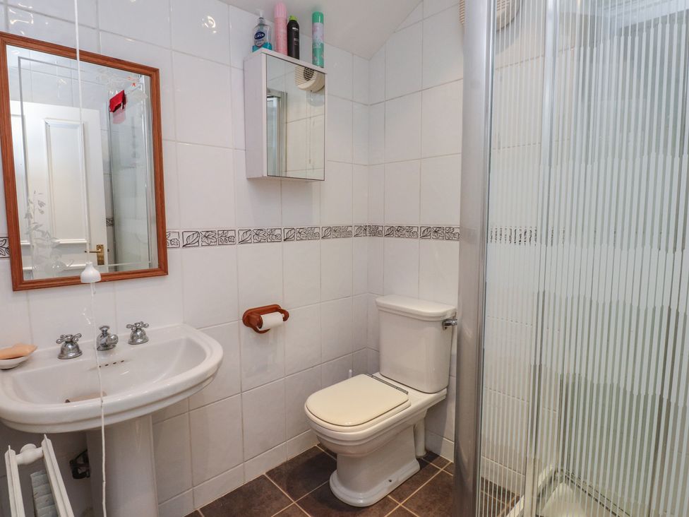 A bathroom with a sink, toilet, shower, and mirror at Bryniau in Pwllheli
