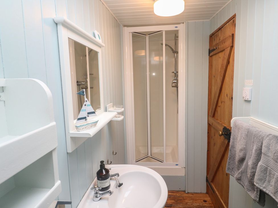 A bathroom with a sink, shower, mirror and wooden door at Pleasans in Hayle